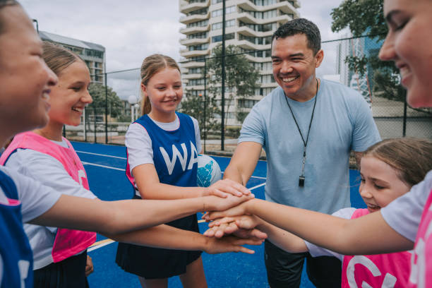 Australian young netball team players huddling stacking hands before the game start with coach