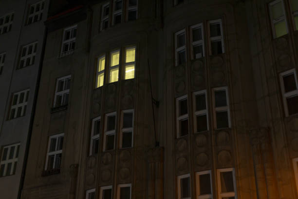 An illuminated window brightly shines on a dark building facade, creating a striking urban scene that beautifully highlights intricate architecture and captivating contrast in lighting