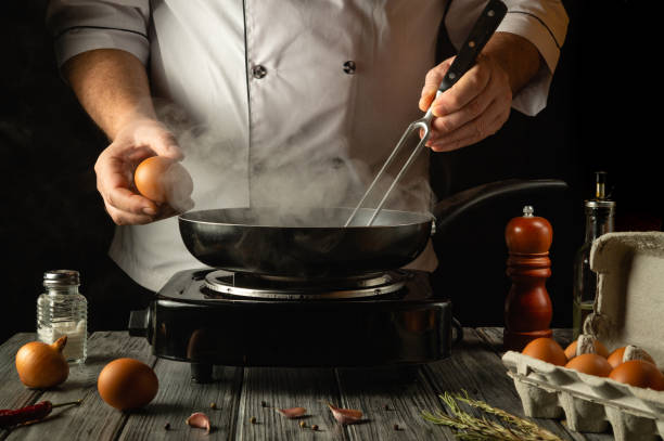 istock A chef prepares to create a tasty dish by cracking fresh eggs into a hot skillet. Steam rises as culinary magic begins at an early hour, accompanied by rustic ingredients on the table 2196022135