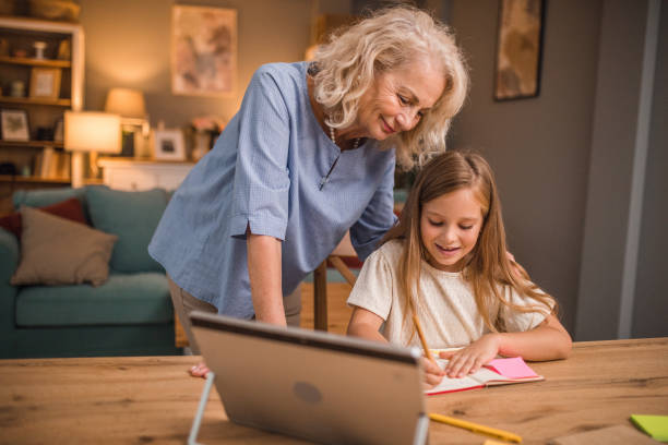 istock A happy grandmother helps her granddaughter while she studies and writes her homework 2196031398