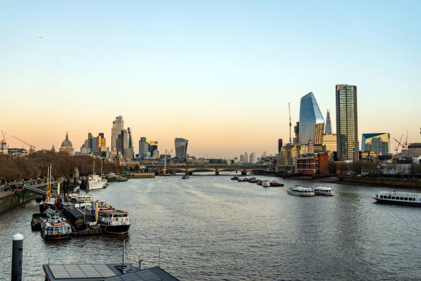 Boats sailing on the thames river with the london skyline reflecting at sunset