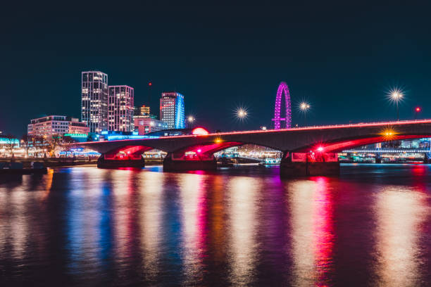 Colorful cityscape of london at night, featuring a bridge illuminated in pink and the london eye ferris wheel