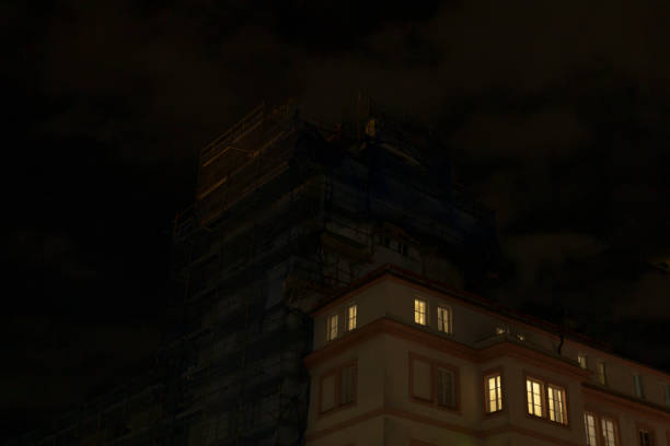 A captivating view of a tall building that is currently undergoing renovation at night, featuring illuminated windows that stand out against the backdrop of a dark and cloudy sky