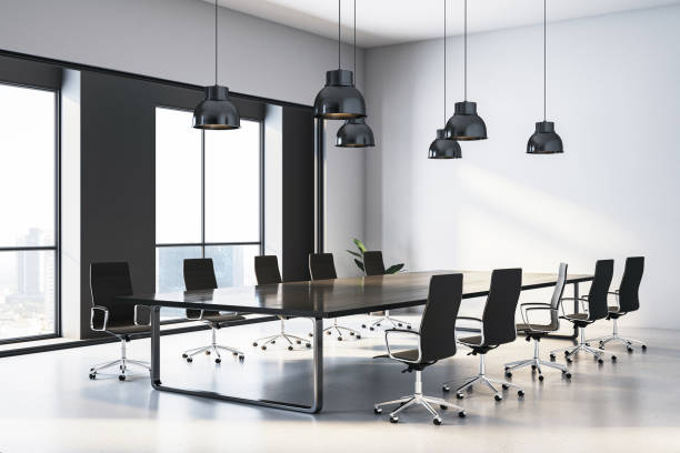 istock Modern conference room with empty black chairs around a large wooden table and industrial pendant lights in a bright office building. 3D Rendering 2196039308