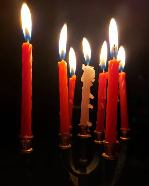istock Candles burning in a menorah with red and white wax dripping in a dark setting 2196043038