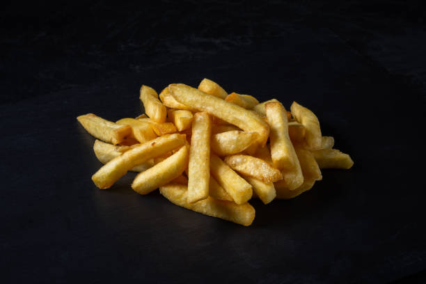 istock French fries piled on stone cutting board on black background. side angle view. fast food photography 2196043243