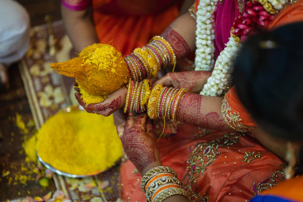 Bride holding a coconut with rice as a base on her palms, while a bridesmaid ties a thread on her hand during the wedding ceremony.