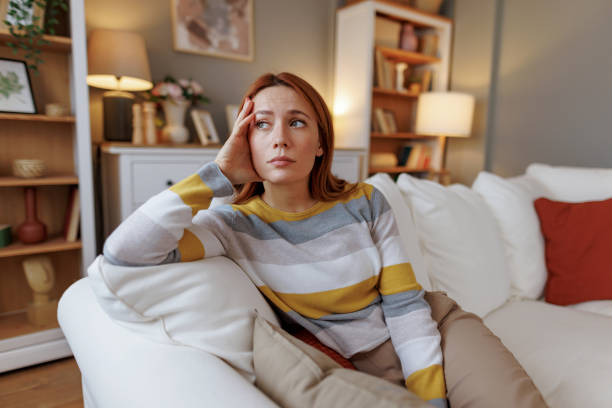 istock Young woman sitting on sofa looking pensive and thoughtful 2196048895