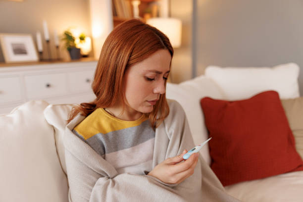 istock Sick young woman checking her temperature on a digital thermometer at home 2196049019