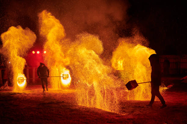 Silhouette of two fire performers with sparkling fire staff erupting in night sky, showcasing energy and artistry of fire manipulation during an outdoor fire show