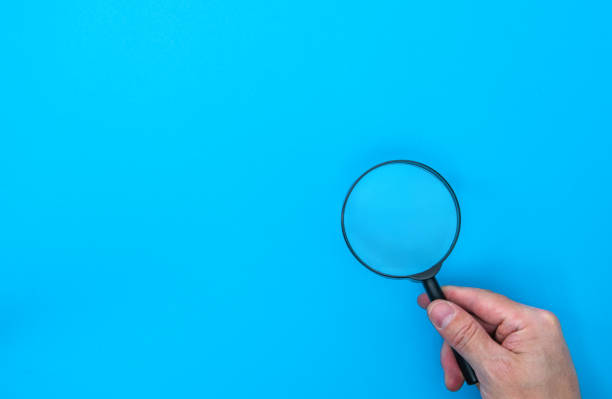 istock Man hand holding a magnifying glass on blue background 2196056295