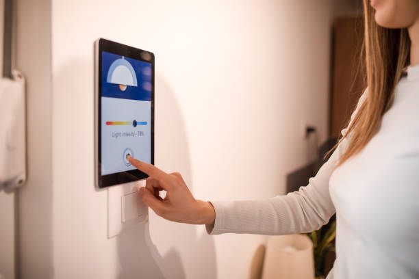 istock Young woman controlling home light son smart home app on device attached on wall 2196059667
