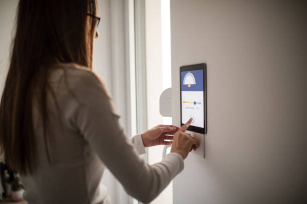 istock Young woman controlling home light son smart home app on device attached on wall 2196059694