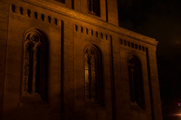As night falls, the stained glass windows and intricate stonework of the gothic church create a captivating atmosphere under the serene, starry sky, evoking timeless beauty