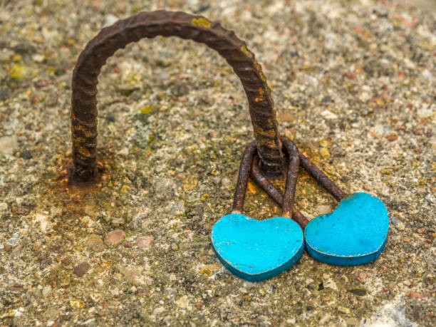 Blue heart-shaped padlocks symbolize unity and love, secured on a weathered metal loop. Surrounded by textured concrete, this evokes themes of romance, commitment, and the strength of bonds over time.