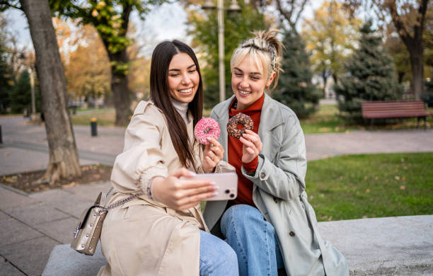 istock Female friends taking selfies while eating donuts 2196071430