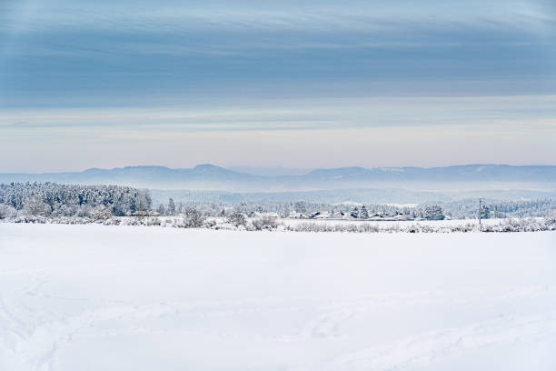 A snowy field with a mountain in the background. The sky is blue and cloudy. There are no people or animals visible in the image