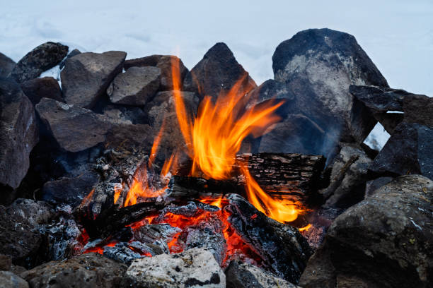Campfire Burning in Fire Ring in Winter with Snow - Dusk blue hour with flames and heat in cold mountain environment.  Blue hour with glowing fire at campsite. Rock fire ring and orange flames.