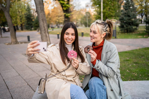 istock Female friends taking selfies while eating donuts 2196071835