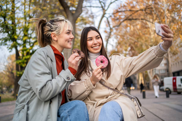 istock Female friends taking selfies while eating donuts 2196071985