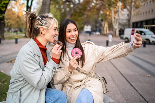 istock Female friends taking selfies while eating donuts 2196072224