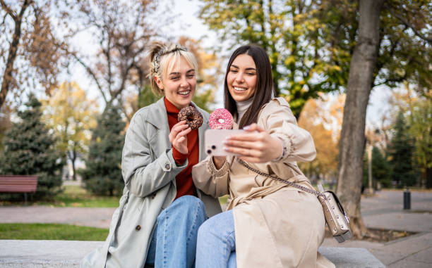 istock Female friends taking selfies while eating donuts 2196072622