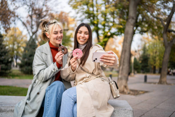 istock Female friends taking selfies while eating donuts 2196072769