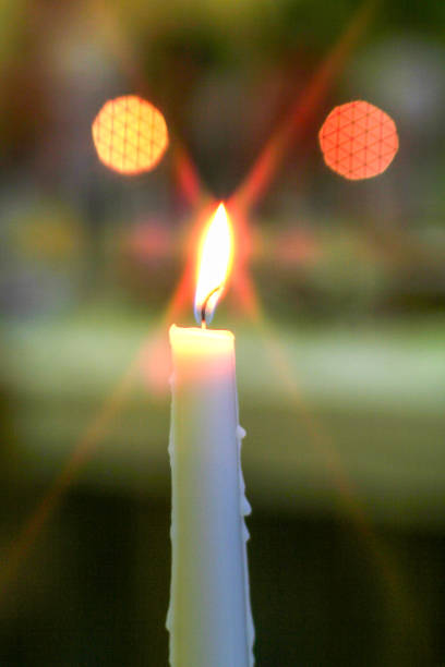 A candle is lit and the light is shining on it. The candle is white and the light is orange