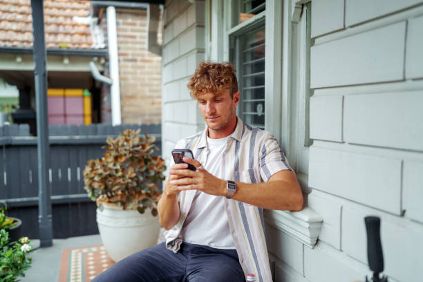 istock Young handsome man text messaging while sitting in front of his home 2196080389