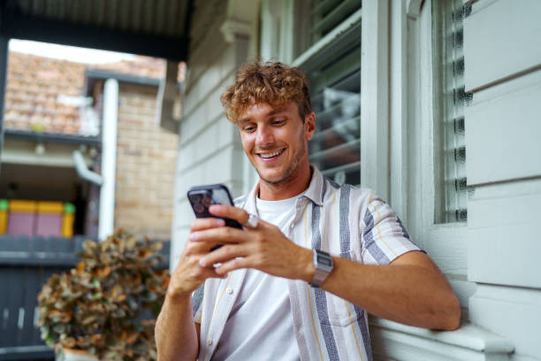 Cheerful handsome man text messaging while sitting front of his house