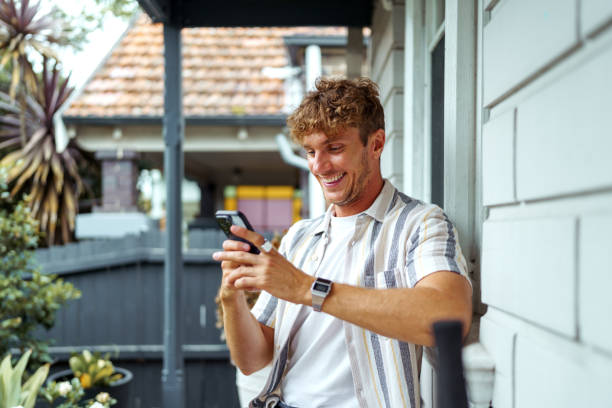 istock Cheerful handsome man text messaging while sitting front of his house 2196080627