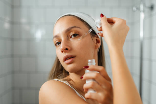 young woman applying facial serum in a modern bathroom - tratamento de pele imagens e fotografias de stock
