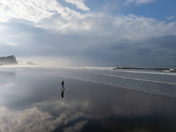 istock Solitary Figure Walking Along Tranquil Beach at Sunrise 2196085548