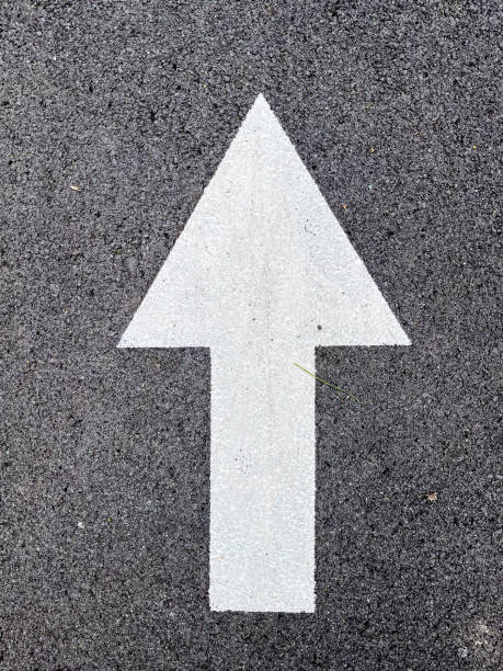 istock A bright white arrow painted on black asphalt indicating forward direction on a road 2196104234