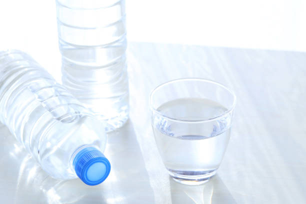 Water of plastic bottle and glass on a wooden table with the morning bright sun shining on the background