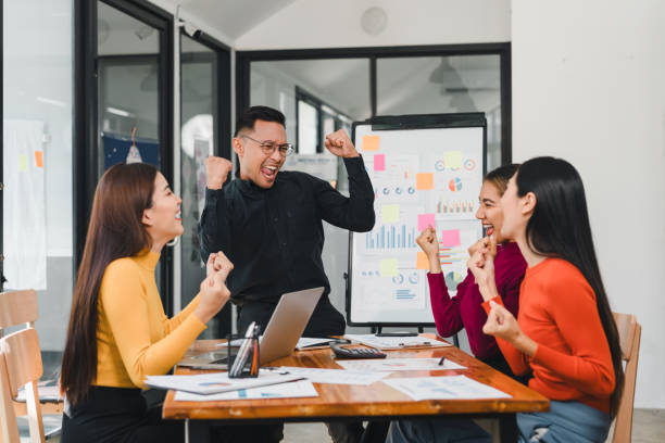 istock Team celebrating success in modern office, showcasing joy and teamwork. group is engaged, with charts and documents on table, highlighting collaboration and achievement 2196110678