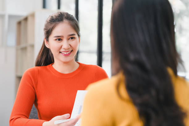 istock young woman in bright orange sweater smiles while engaging in conversation with another person. setting is modern and inviting, perfect for collaboration 2196111285