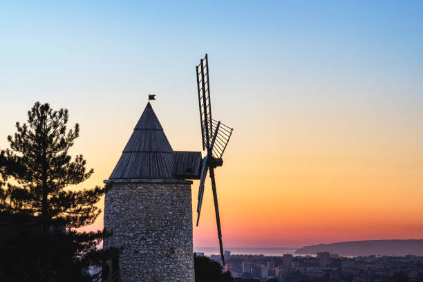 A traditional stone windmill with wooden blades standing in a vibrant green field under a clear blue sky.