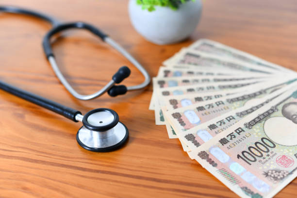 机の上には聴診器と大量の日本紙幣が並んでいます - 給付金 ストックフォトと画像