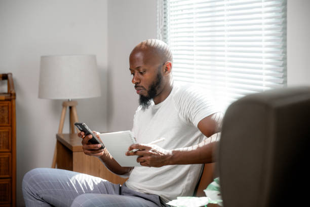 istock Young adult black man working from home, checking his phone and taking notes on a notepad 2196121038
