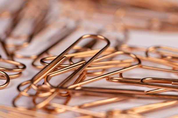 orange paper clips made of metal for the systematization of documents and paper, large  sized copper paper clips lie on white blank paper