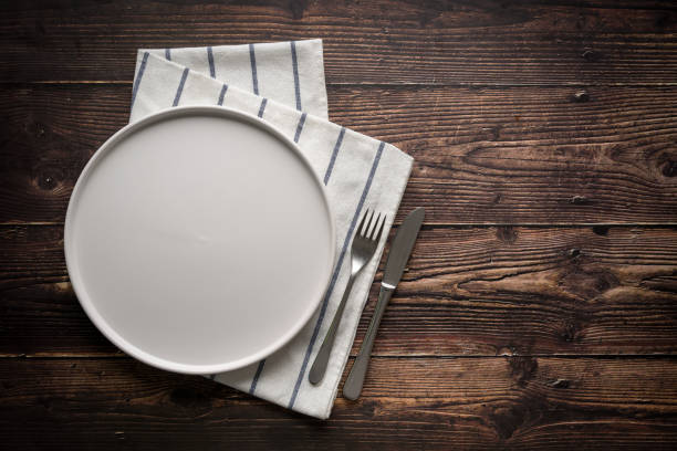 istock Top view of empty ceramic white plate, fork and table knife on wooden table 2196132144