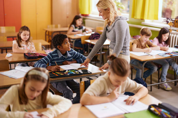 istock Happy elementary teacher assisting black schoolboy on a class. 2196132472
