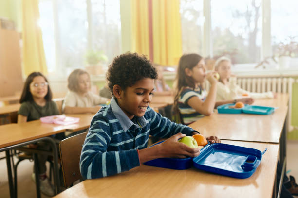 Happy black boy having fruit for snack during a break in the classroom.