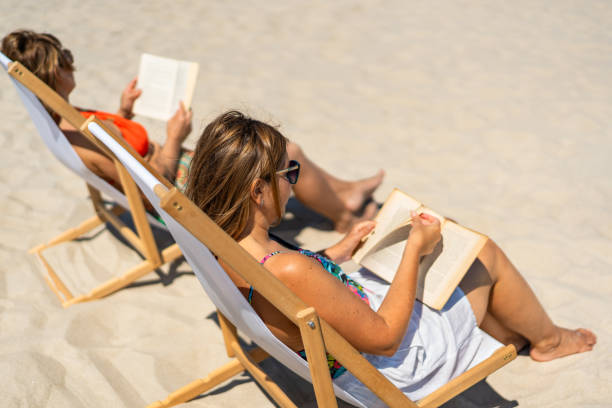 istock Two mature women reading books sitting on deckchairs on beach 2196132794