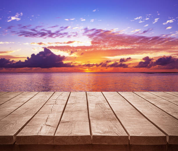 Empty wooden table top with tropical ocean sunset and dramatic sky background