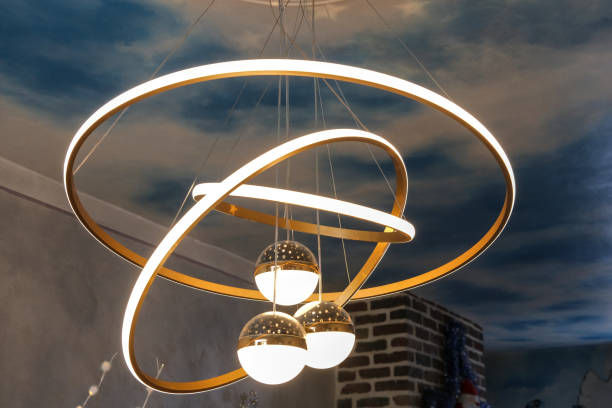istock A modern chandelier with three glowing bulbs is suspended from a ceiling painted to resemble a cloudy sky. 2196139727
