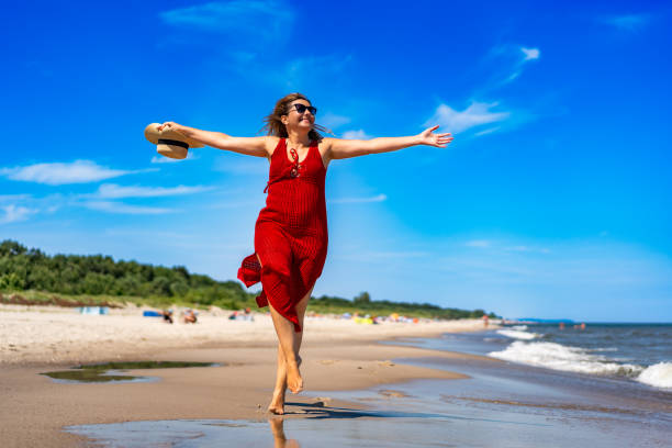 istock Smiling mature woman running on sandy beach 2196141232