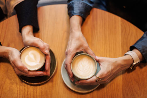 istock Two women holding latte art coffee cups at cafe table 2196142946