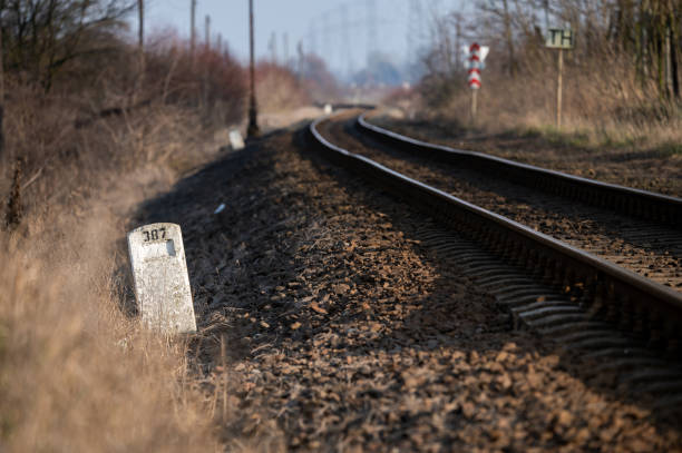 A scenic view of curving railway tracks flanked by bare shrubs and power line towers in the background. The rustic setting highlights transportation and energy infrastructure in a rural environment.